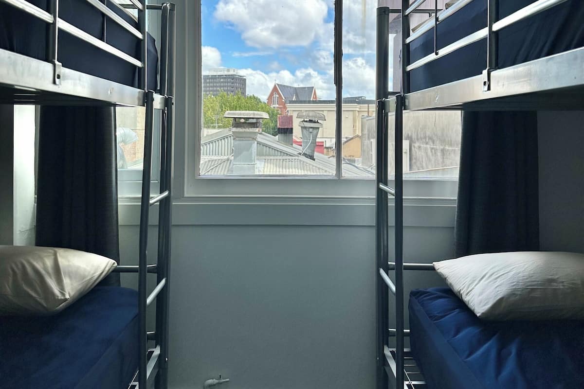 Ein Schlafsaalzimmer mit Etagenbetten, einem Fenster mit Blick auf Gebäude und eine Brücke sowie einem kleinen Fensterbrett.