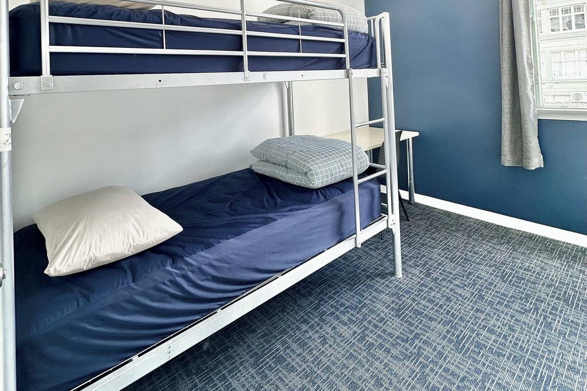 Ein Schlafraum mit Etagenbett, Fenster, kleinem Tisch und Teppichboden.