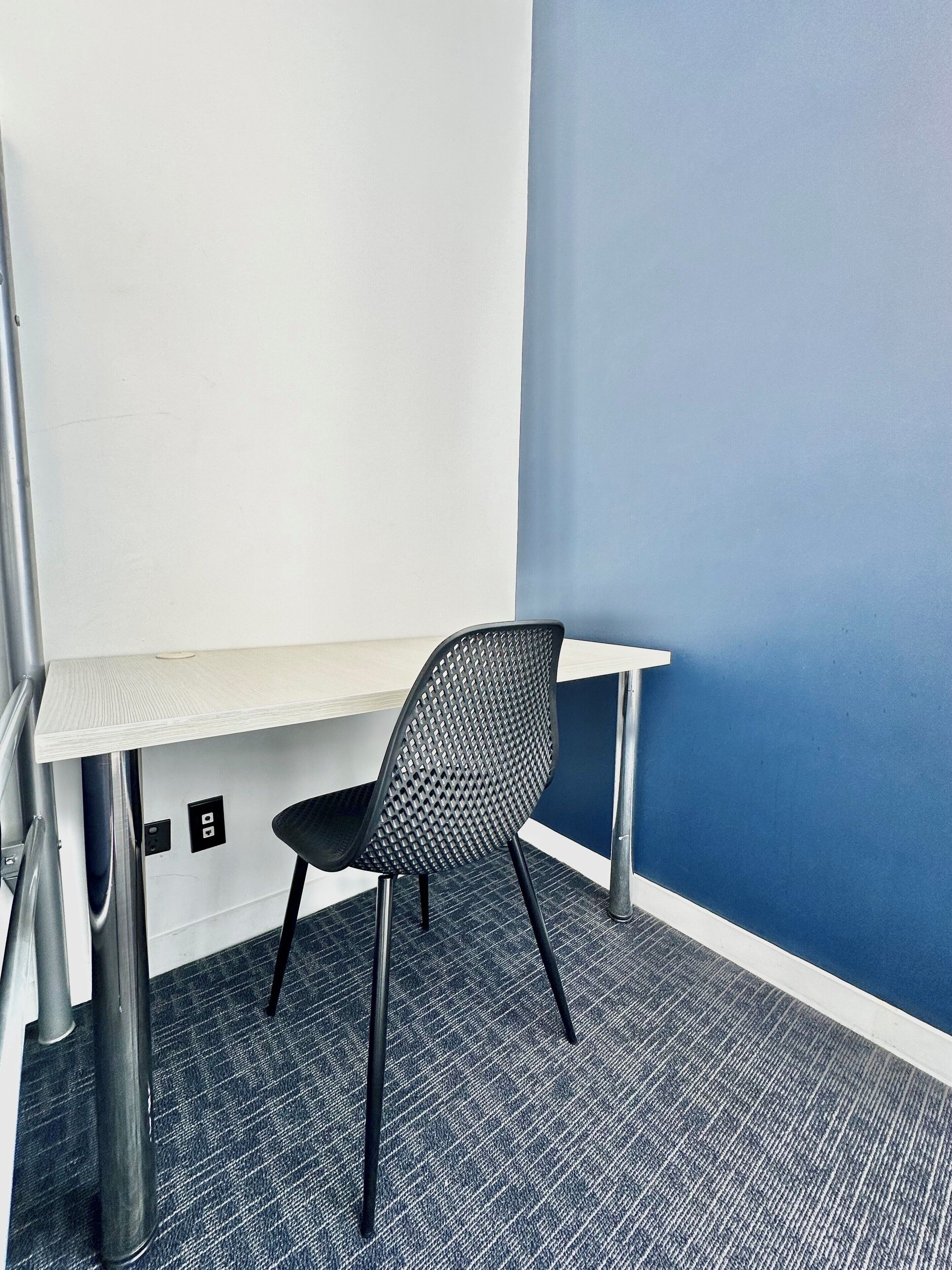 Oficina en esquina con escritorio blanco, silla de malla negra y una pared de acento azul.