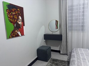 A bedroom with a bed, a bedside table, a mirror, a small stool, and a painting on the wall. - Sky View 1-bedroom apartment in the heart of Kampala (Kampala)