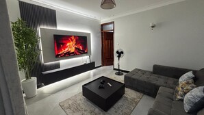 A modern living room with a flat-screen TV, a black coffee table, a grey sofa, and a potted plant. - Sky View 1-bedroom apartment in the heart of Kampala (Kampala)
