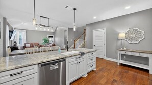 A modern kitchen with a large island, white cabinetry, and a dishwasher. - Conroe 4BR near The Woodlands | Arcade Game Room, Gym, Playground, Sleeps 13 (Conroe)