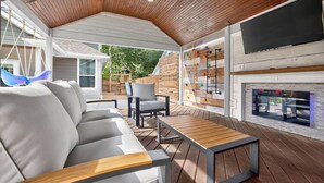 An outdoor patio with a wooden ceiling, a sofa, a chair, a table, a climbing wall, and a fireplace. - Conroe 4BR near The Woodlands | Arcade Game Room, Gym, Playground, Sleeps 13 (Conroe)
