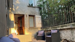 A room with a bed, two wicker chairs, a small table, and a view of a bamboo fence.