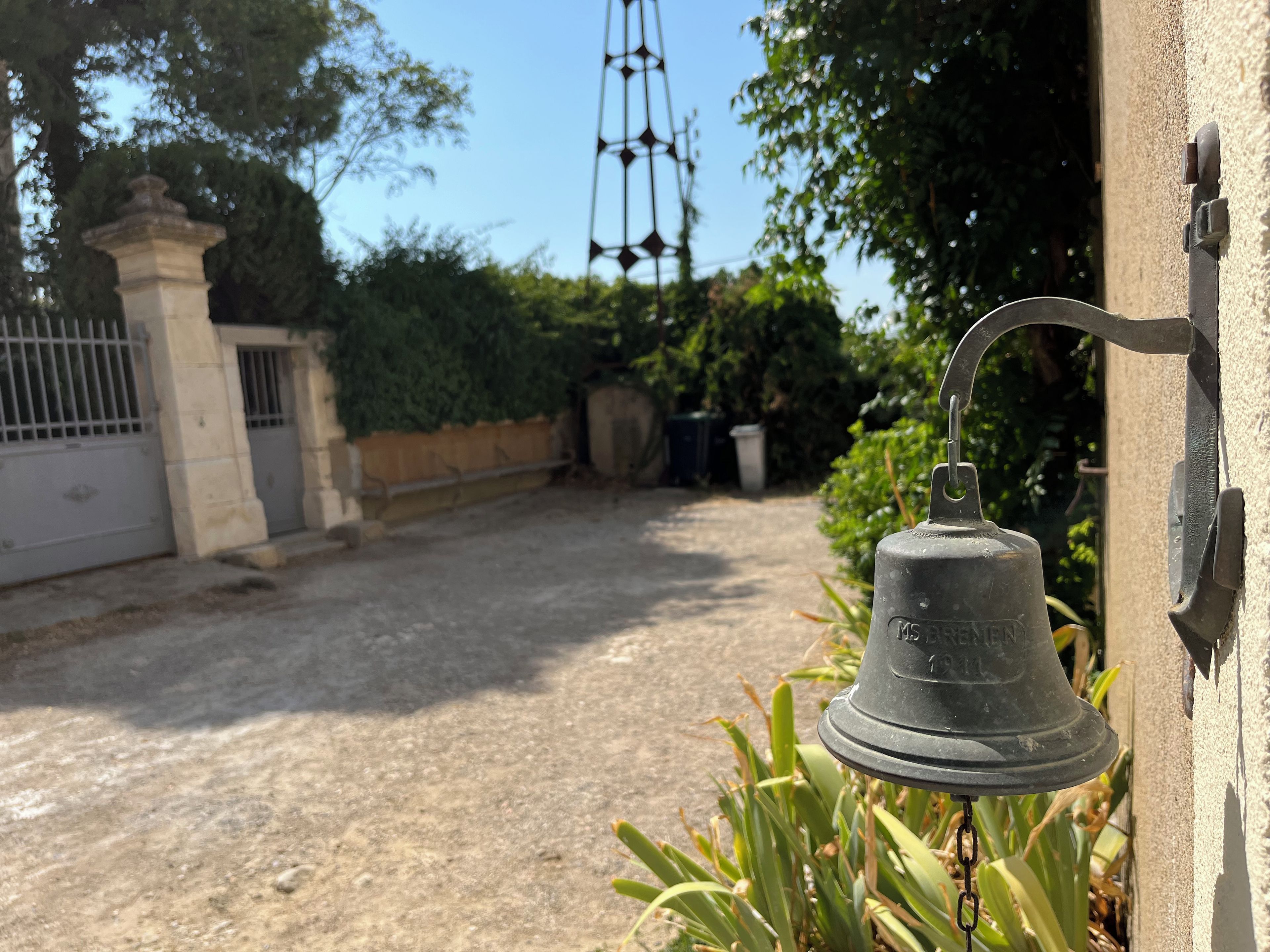 A bell mounted on a wall, a gated entrance, and a pathway leading to a building.