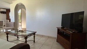 A living room with a television on a wooden stand, a glass coffee table, and a sofa.