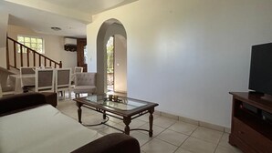 A living room with a sofa, a glass coffee table, a TV stand, and a staircase leading to another room.