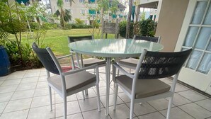 A patio with a glass table and four chairs, surrounded by a garden and a building with balconies. - Garden-Sea view, 2 bedroom/2bath Montego Freeport (Montego Bay)