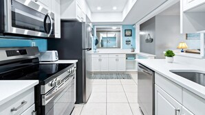 A modern kitchen with stainless steel appliances, white cabinetry, and a blue accent wall. - Oceanfront 2BR Condo with Large Balcony & Beach Access! 🌴 (Satellite Beach)