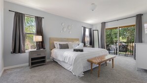 Un dormitorio con cama, mesita de noche, lámpara y vistas al exterior a través de amplios ventanales.