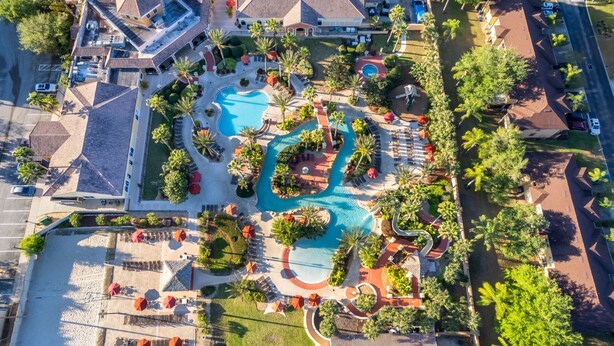 Vista a érea de un complejo turístico con una piscina central, varias edificaciones y zonas ajardinadas.