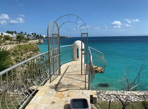 A staircase leading to a beach with clear turquoise water, a metal railing, and a view of the ocean. - Caribbean Getaway: 2BR Condo at Rainbow Beach Club (Cupecoy)