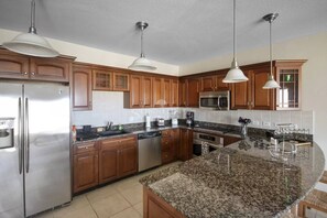 A modern kitchen with wooden cabinets, stainless steel appliances, and a granite island. - Caribbean Getaway: 2BR Condo at Rainbow Beach Club (Cupecoy)