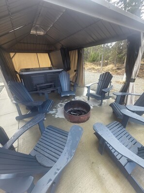 A covered outdoor seating area with Adirondack chairs, a fire pit, and a table with chairs. - Seren hideaway minutes from the best Salmon fishing in Alaska! (Soldotna)