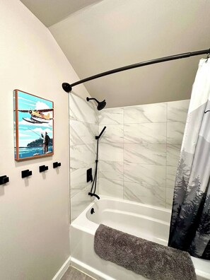 A bathroom with a bathtub, a showerhead, a towel rack, and a framed picture on the wall. - Seren hideaway minutes from the best Salmon fishing in Alaska! (Soldotna)