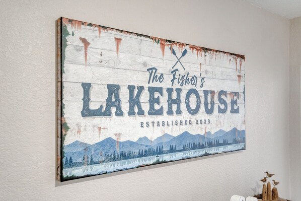 Ein rustikales Schild mit dem Text „The Fisher's Lakehouse Gegründet 2029“ und einer Illustration einer Berglandschaft.