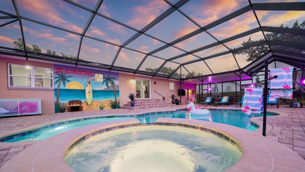 Ein Innenpool mit tropischem Wandbild, eine Whirlpoolanlage und eine überdachte Terrasse.
