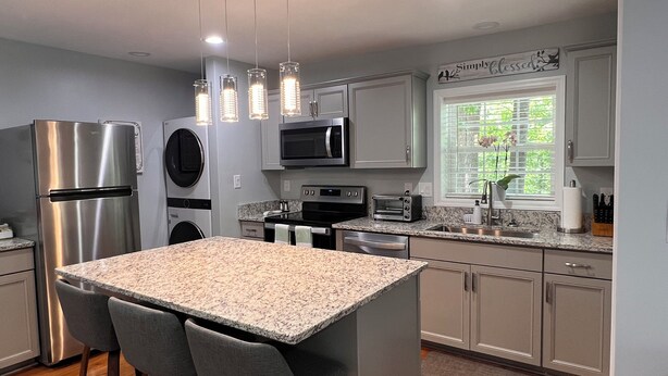A modern kitchen with stainless steel appliances, granite countertops, and a central island with seating. - Private, secure and serene getaway at Oak Grove Cottage! (Arden)