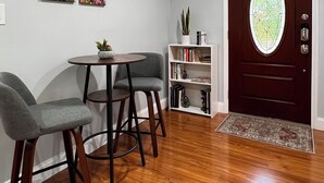 A dining area with a round table and two chairs, a bookshelf, and a door with a glass panel. - Private, secure and serene getaway at Oak Grove Cottage! (Arden)