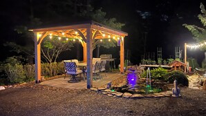 A gazebo with string lights, outdoor seating, a grill, and a small water feature. - Private, secure and serene getaway at Oak Grove Cottage! (Arden)