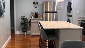 A modern kitchen with a central island, stainless steel appliances, and a dining area with a round table and chairs. - Private, secure and serene getaway at Oak Grove Cottage! (Arden)