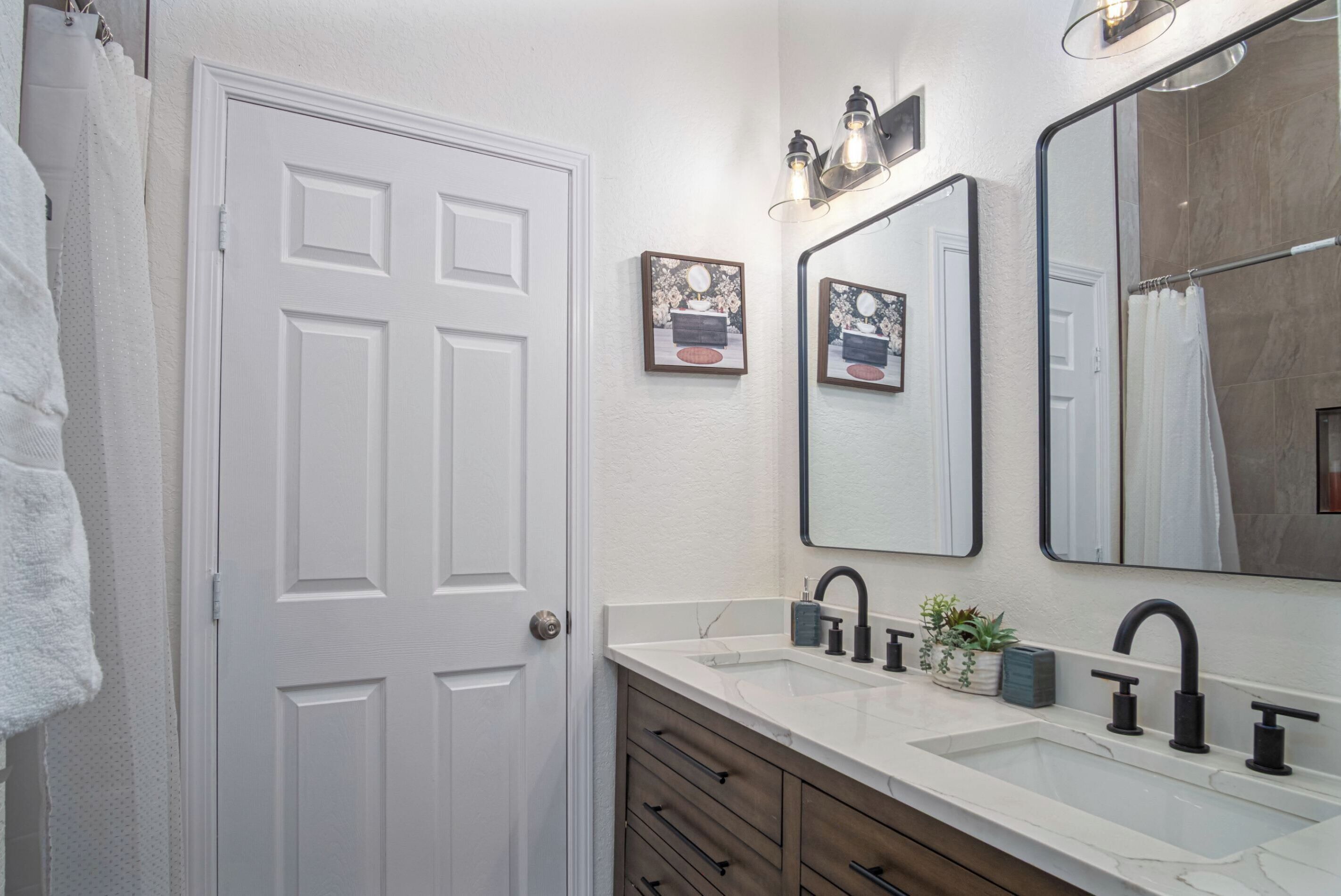 A bathroom with a white door, two wall-mounted mirrors, a sink with black faucets, and a towel rack with a white towel.
