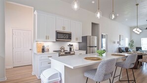 Una cucina moderna con mobili bianchi, elettrodomestici in acciaio inossidabile e un'isola centrale con sgabelli da bar.