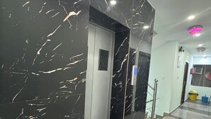 Een hal met een wand van zwart marmer en een deur die naar een kamer leidt. De vloer is betegeld met een ruitpatroon.