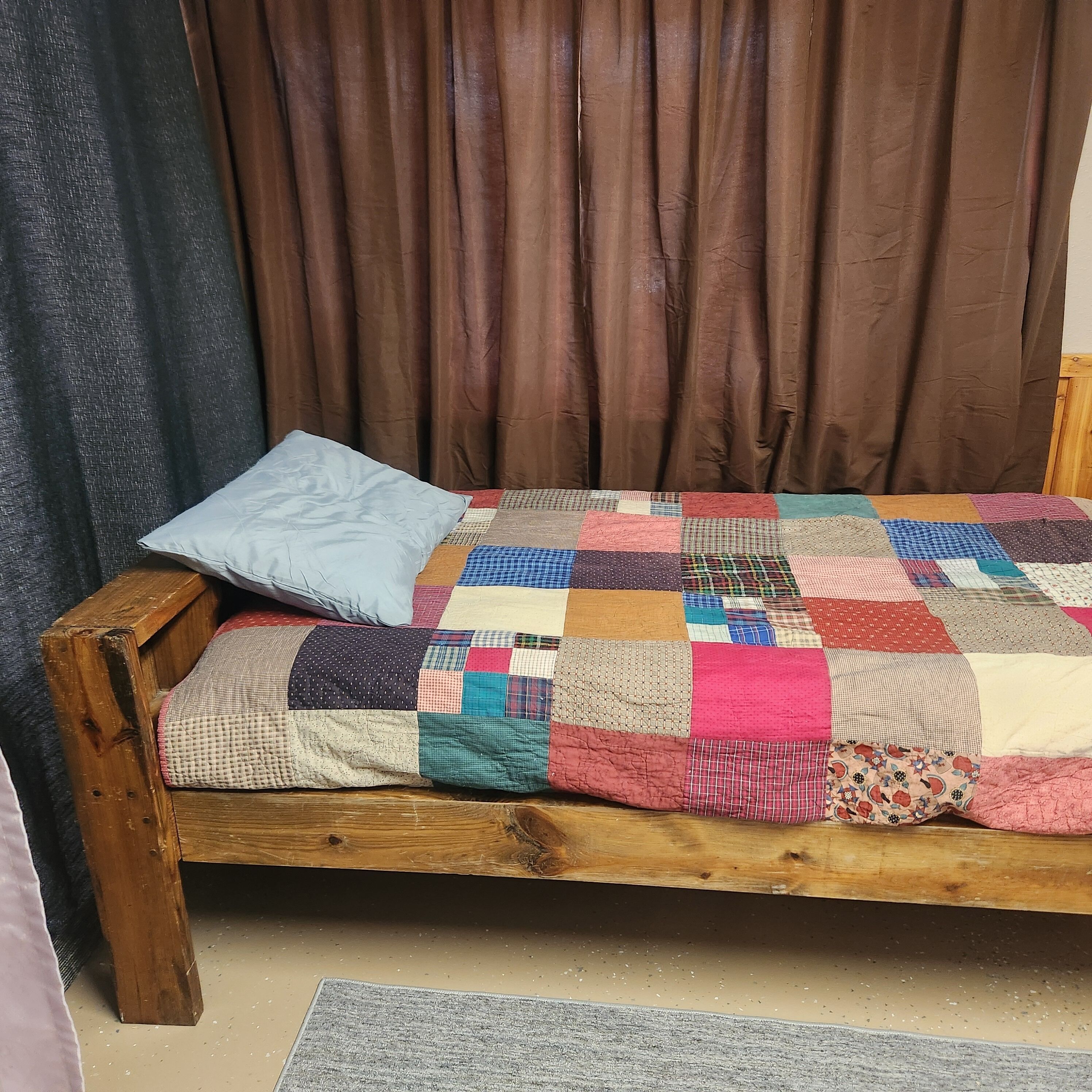 A wooden bed with a colorful patchwork quilt and a single pillow.