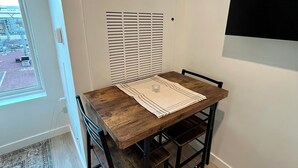 Un petit coin repas avec une table et des chaises en bois, un tapis à motifs et une fenêtre avec des stores.