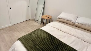 Une chambre à coucher avec un lit, un tabouret rond en bois, un miroir et une porte blanche.