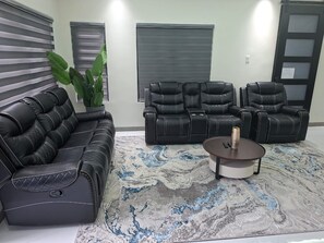 Een woonkamer met een bank, twee fauteuils, een salontafel en een grote potplant.