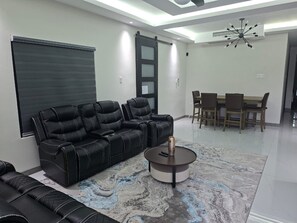 Een moderne woonkamer met een zwarte leren bank, een ronde salontafel en een eethoek met houten stoelen.
