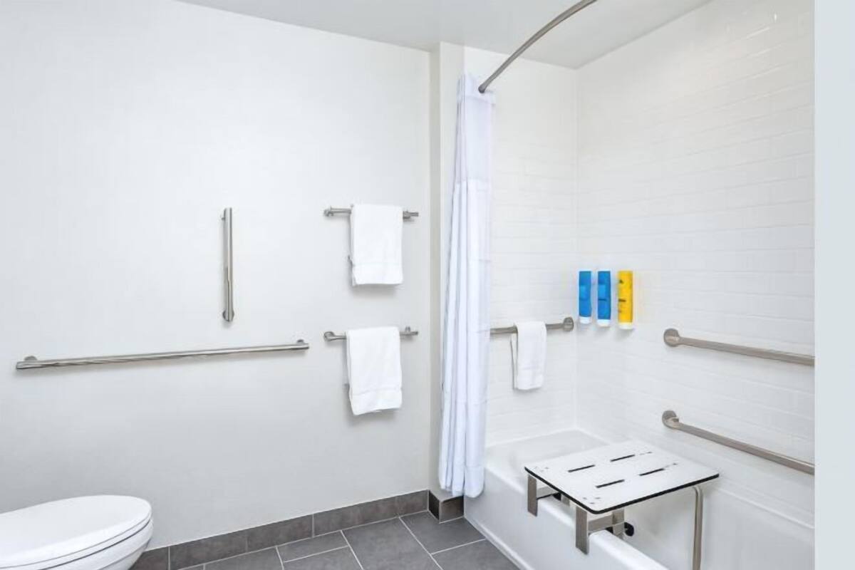Ein Badezimmer mit Toilette, Dusche mit Vorhang, Haltegriffen und einem Händetrockner.