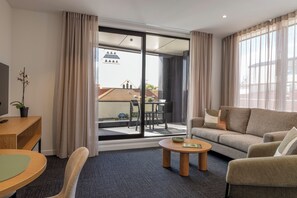 En moderne stue med sofa, sofabord, TV og en balkon med udsigt.