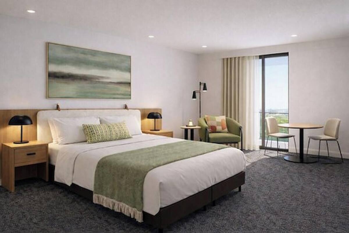 A hotel room with a bed, bedside tables, a desk, a chair, a round table, and a large window.