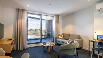 A modern hotel room with a sofa, a desk, a laptop, and a dining table.