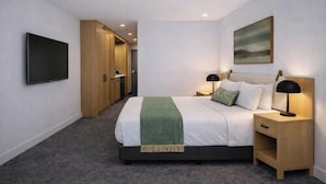 A hotel room with a bed, bedside tables, a TV, a painting, and a carpeted floor. - Quest Havelock North (Havelock North)