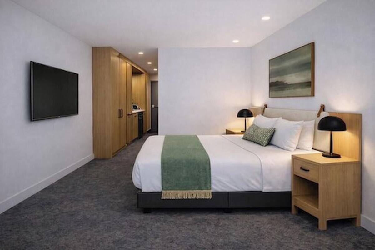 A hotel room with a bed, bedside tables, a TV, a painting, and a carpeted floor.