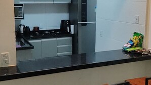 A modern kitchen with a black countertop, stainless steel appliances, and a small refrigerator. There are three wooden stools at the counter. - Comfortable, fully equipped 3-bedroom apartment with garage and 24-hour security. (Belém)