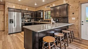 A modern kitchen with dark wood cabinets, stainless steel appliances, and a central island with stools. - Bear Monkey Lodge - Luxury 4 Bedroom with Hot Tub + Fireplaces + Scenic Views! (Sevierville)