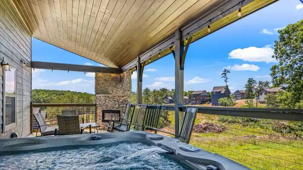 A hot tub area with a stone wall, lounge chairs, and a view of a residential neighborhood. - Bear Monkey Lodge - Luxury 4 Bedroom with Hot Tub + Fireplaces + Scenic Views! (Sevierville)