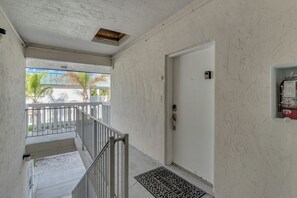Ein Flur mit einer weißen Tür, einem Rauchmelder und Blick auf einen Balkon mit Geländer.