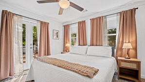 Un dormitorio con cama, dos mesitas de noche, ventilador de techo y vistas al exterior.