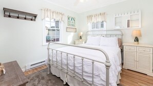 A bedroom with a bed, bedside tables, a nightstand, a ceiling fan, a window with curtains, a wall-mounted shelf, and a mirror. - Gorgeous 3-bedroom house in tranquil Westbrook perfect for relaxing getaway (Westbrook)
