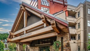 En stuga med en fasad av sten, träbjälkar och en skylt med texten ”LAKE PLACID LODGE”.
