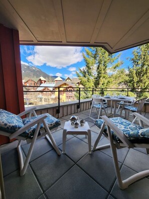 A terrace with lounge chairs and a table, overlooking a mountainous landscape. - Ultimate Creekside Ski Base • Pool, Hot Tub, Sauna (Whistler)