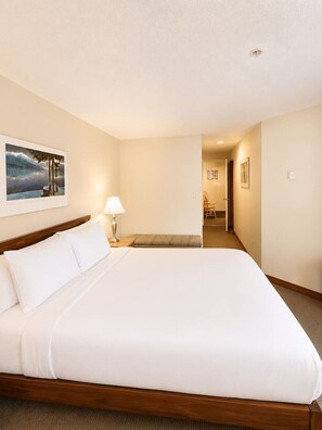 A hotel room with a large bed, a bedside lamp, a picture on the wall, and a hallway leading to another room. - Ultimate Creekside Ski Base • Pool, Hot Tub, Sauna (Whistler)
