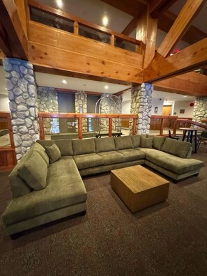 A modern living room with a sectional sofa, a wooden coffee table, and stone walls. - Ultimate Creekside Ski Base • Pool, Hot Tub, Sauna (Whistler)