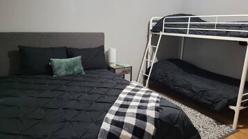 A bunk bed with a checkered blanket, a bedside table with a lamp, and a grey headboard.